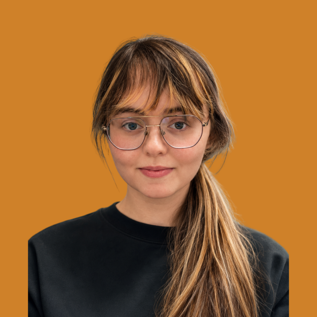 Hannah, Marketing Assistant at Silver Apples Digital, wearing glasses and a black top against an orange background.
